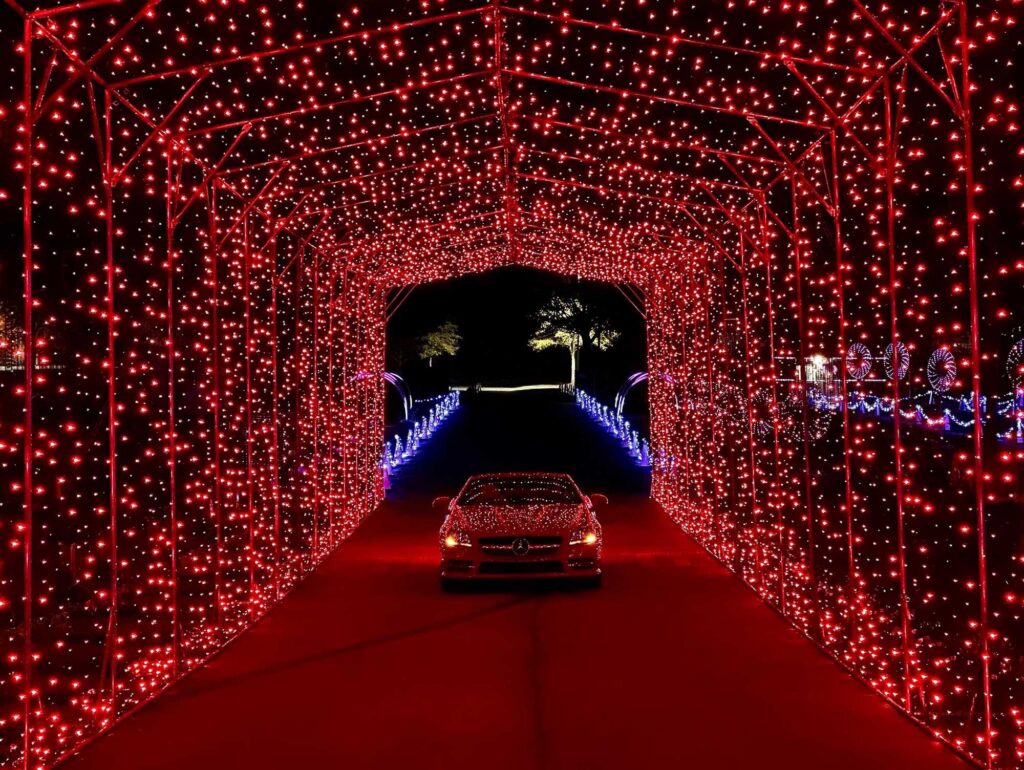 A red convertible car entering the tunnel of red holiday lights.