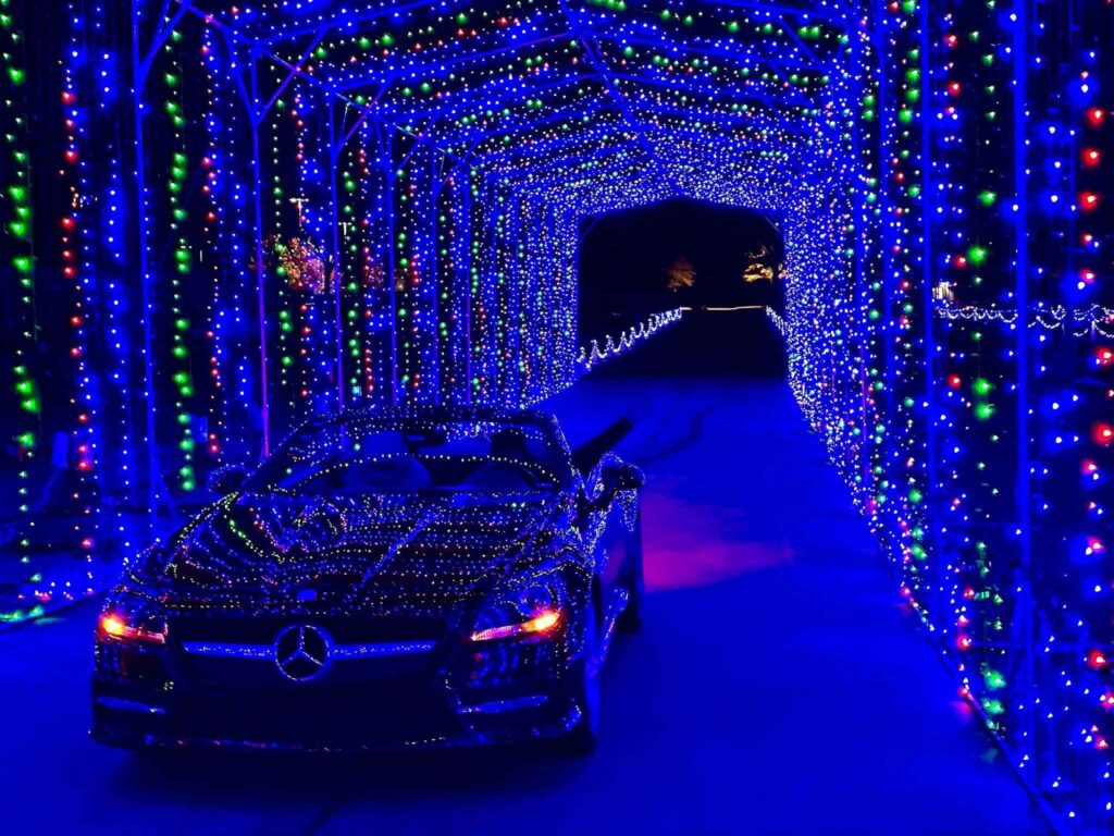 Person driving a convertible through a tunnel of blue lights. Their hand is sticking out of the driver side, waving at the camera.