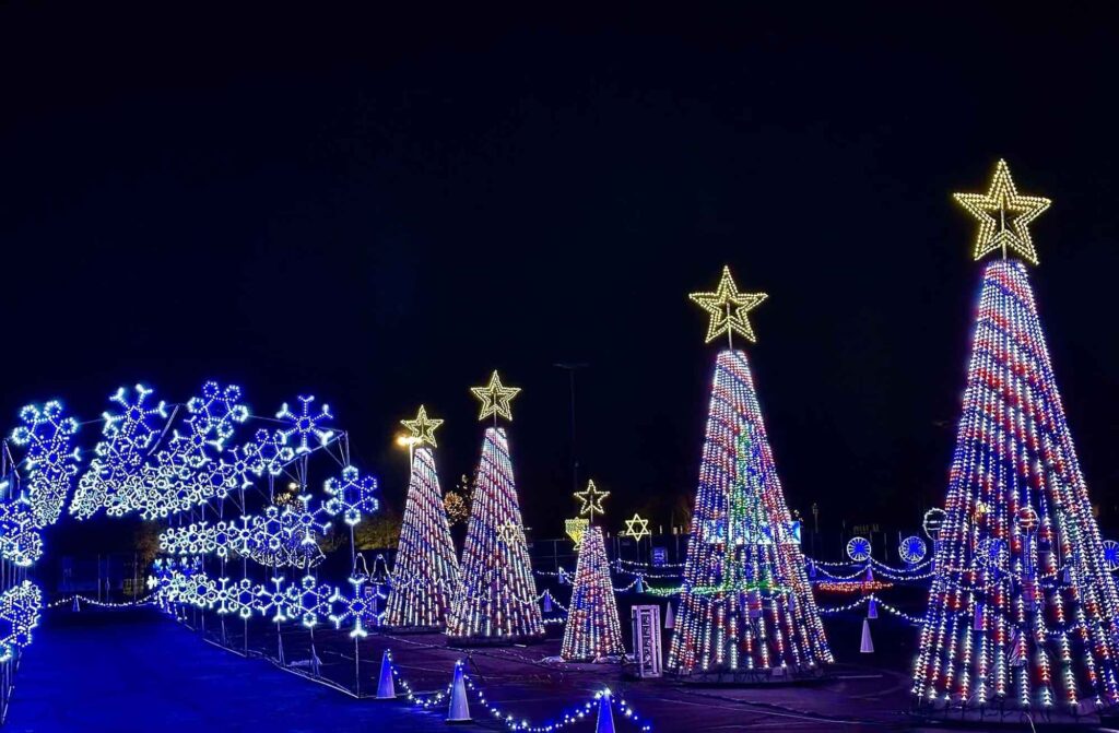 An illuminated snowflake tunnel with snowflake and five light up trees with stars on top.