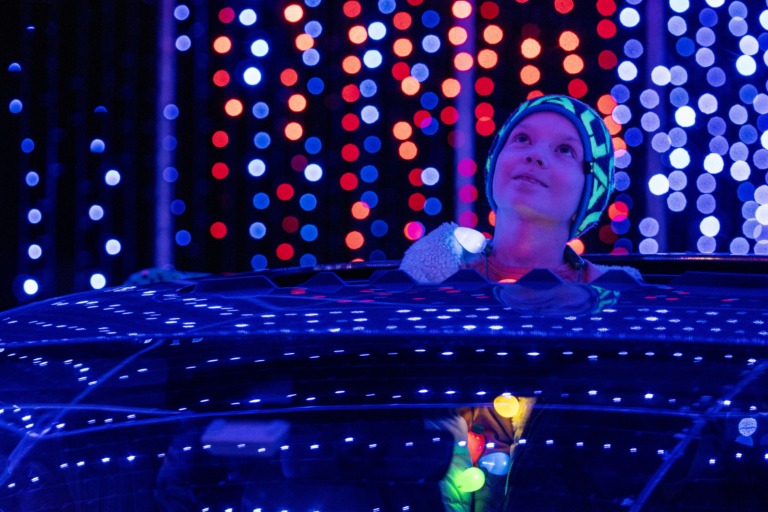 A boy pops his head out the sunroof of the car as they are driving through the holiday light show experience.